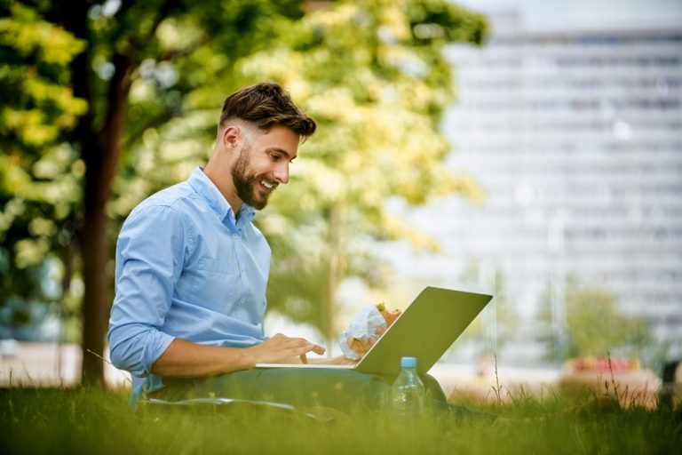 Chico empleando su ordenador portátil para trabajar en su web profesional en el exterior